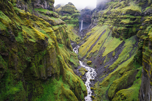 Aerial view of Mulagljufur Canyon with a waterfall cascading down moss covered cliffs into a winding river Eastern Region Iceland. Aerial view of Mulagljufur Canyon with a waterfall cascading down moss covered cliffs into a winding river Eastern Region Iceland.