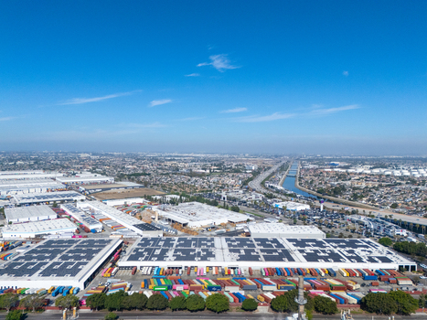 Aerial view of a large industrial logistics facility featuring rows of colorful shipping containers and solar panels on warehouse rooftops in Carson California United States.