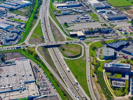 Aerial view of a complex highway interchange weaving through industrial zones and pockets of verdant greenery casting shadows under the bright sun Sausheim Grand Est France.