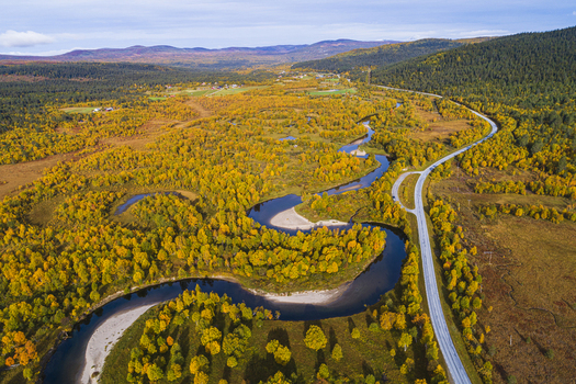 Aerial view of the Ljusnan river winding through a vibrant autumn forest with golden trees and a road running alongside in the valley of Bruksvallarna Jamtland County Sweden. Aerial view of the Ljusnan river winding through a vibrant autumn forest with golden trees and a road running alongside in the valley of Bruksvallarna Jamtland County Sweden.
