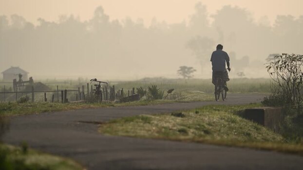 View of a man cycling on a rural road in foggy morning Bangladesh.