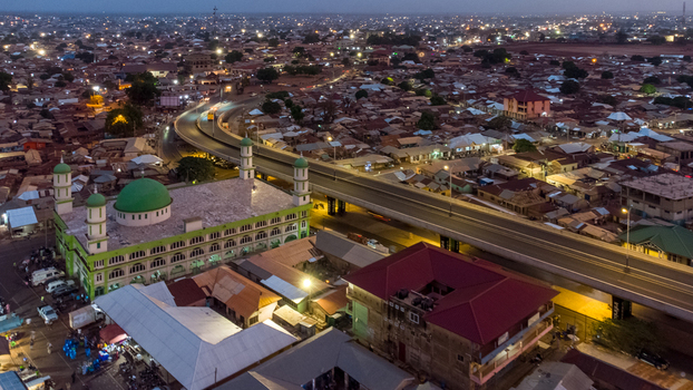 Aerial view of the Tamale Central Mosque illuminated at twilight situated next to an elevated highway with urban sprawl and street lights in Tamale Northern Region Ghana. Aerial view of the Tamale Central Mosque illuminated at twilight situated next to an elevated highway with urban sprawl and street lights in Tamale Northern Region Ghana.