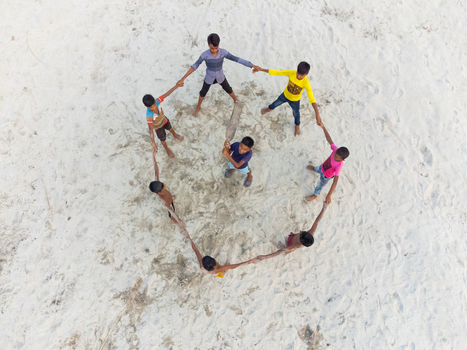 Alakjhari Bangladesh 26 July 2026 Aerial view of children holding hands in a circle around a boy with a cricket bat on the sandy banks of Jharbari ghat.