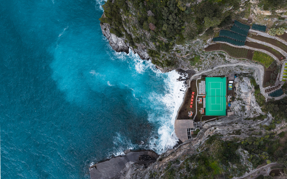 Aerial view of turquoise waters crashing against rugged cliffs near 2 Via Laurito contrasting with the green rooftops and terraced landscapes Laurito Campania Italy. Aerial view of turquoise waters crashing against rugged cliffs near 2 Via Laurito contrasting with the green rooftops and terraced landscapes Laurito Campania Italy.