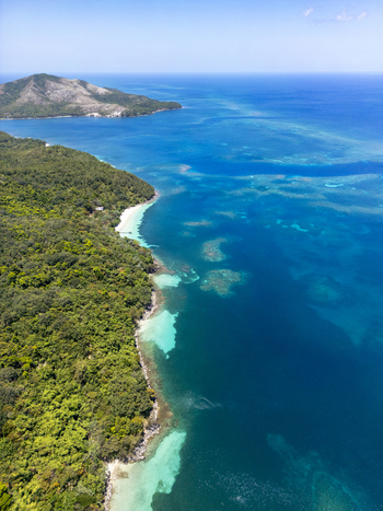 Aerial view of lush green hills meeting the turquoise Caribbean Sea with visible coral reefs and a clear blue sky Guanaja Bay Islands Department Honduras. Aerial view of lush green hills meeting the turquoise Caribbean Sea with visible coral reefs and a clear blue sky Guanaja Bay Islands Department Honduras.