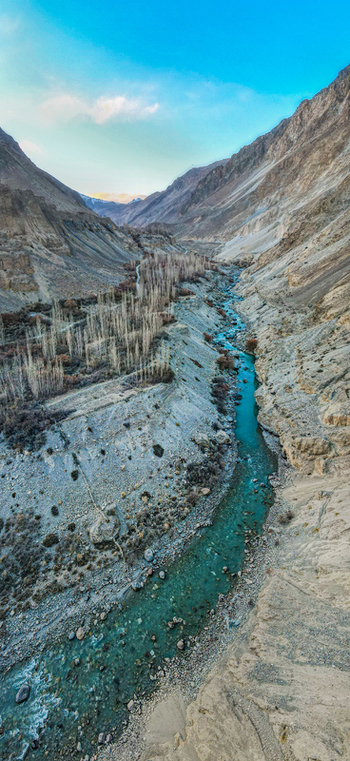Aerial view of a vibrant turquoise river carves its way through a rugged mountainous valley near distinctive rock formations Hunza Nagar Gilgit Pakistan. Aerial view of a vibrant turquoise river carves its way through a rugged mountainous valley near distinctive rock formations Hunza Nagar Gilgit Pakistan.