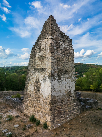 Aerial view of the medieval stone ruins of Csabdi Church with weathered masonry and dry ground above wooded countryside and homes in Csabdi Hungary below a blue sky.
