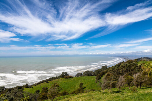 View of Ohope Beach with rolling green hills crashing waves and wispy clouds in the sky in Ohope Bay of Plenty Region New Zealand. View of Ohope Beach with rolling green hills crashing waves and wispy clouds in the sky in Ohope Bay of Plenty Region New Zealand.