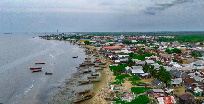 Aerial view of Bonny Island showing the coastal town with numerous wooden boats moored along the sandy shoreline residential buildings and lush greenery in Bonny Town Rivers Nigeria. Aerial view of Bonny Island showing the coastal town with numerous wooden boats moored along the sandy shoreline residential buildings and lush greenery in Bonny Town Rivers Nigeria.