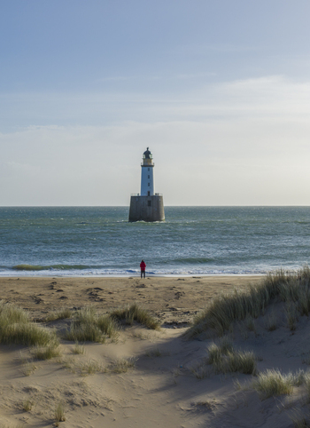 Aerial view of Rattray Head Lighthouse rising from the sea with a person standing on the sandy beach and dunes in Peterhead Scotland United Kingdom. Aerial view of Rattray Head Lighthouse rising from the sea with a person standing on the sandy beach and dunes in Peterhead Scotland United Kingdom.