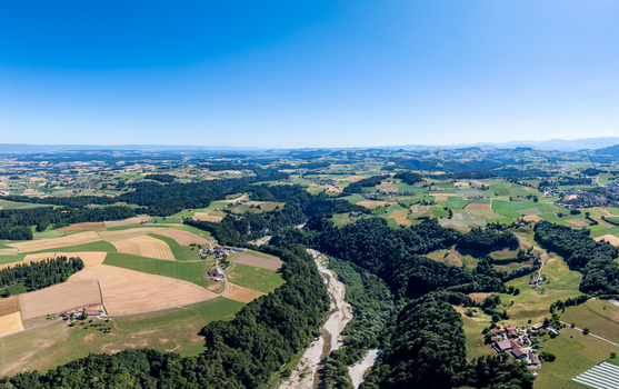 Aerial view of the Sodbachbrucke Sense area featuring a winding river gorge lush green forests and agricultural fields under a clear blue sky in Heitenried Freiburg Switzerland. Aerial view of the Sodbachbrucke Sense area featuring a winding river gorge lush green forests and agricultural fields under a clear blue sky in Heitenried Freiburg Switzerland.