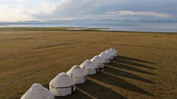Aerial view of a row of traditional yurts set in the vast grassy plains near Song Kul lake under a dramatic sky in Naryn Region Kyrgyzstan. Aerial view of a row of traditional yurts set in the vast grassy plains near Song Kul lake under a dramatic sky in Naryn Region Kyrgyzstan.