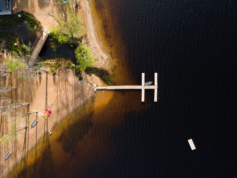 Aerial view of a wooden dock extending into the dark waters of Commanda Lake with a sandy shoreline lush green trees and a small bridge in Restoule Ontario Canada. Aerial view of a wooden dock extending into the dark waters of Commanda Lake with a sandy shoreline lush green trees and a small bridge in Restoule Ontario Canada.
