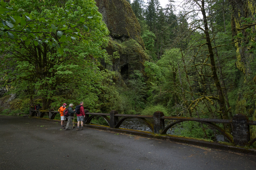 View of hikers standing on a historic stone bridge surrounded by lush mossy forest towering rocky cliffs and a stream in Hood River Oregon United States.