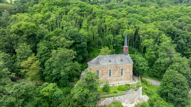 Aerial view of St. Menas church with its stone walls and slender spire surrounded by lush green trees on a hillside in Koblenz Rheinland Pfalz Germany. Aerial view of St. Menas church with its stone walls and slender spire surrounded by lush green trees on a hillside in Koblenz Rheinland Pfalz Germany.
