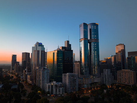 Aerial view of the Melbourne skyline at sunset featuring modern glass skyscrapers reflecting the golden light with urban streets and parkland below in Melbourne Victoria Australia.
