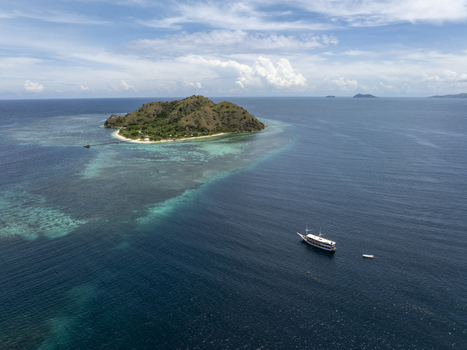 Aerial view of Kanawa Island surrounded by turquoise coral reefs and deep blue sea with a traditional wooden boat anchored nearby in Kecamatan Komodo Nusa Tenggara Timur Indonesia. Aerial view of Kanawa Island surrounded by turquoise coral reefs and deep blue sea with a traditional wooden boat anchored nearby in Kecamatan Komodo Nusa Tenggara Timur Indonesia.