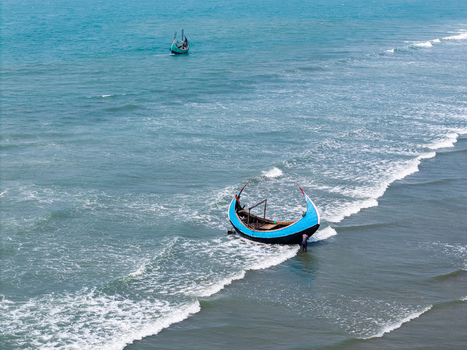 Cox s Bazar Bangladesh 10 March 2026 Aerial view of traditional moon shaped fishing boats on the turquoise waters of the Bay of Bengal with a fisherman pushing a boat into the surf. Cox s Bazar Bangladesh 10 March 2026 Aerial view of traditional moon shaped fishing boats on the turquoise waters of the Bay of Bengal with a fisherman pushing a boat into the surf.