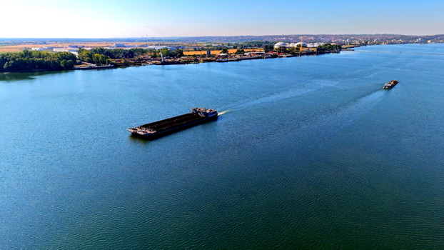 Aerial view of cargo barges navigating the Danube river near the historic Smederevo fortress with industrial infrastructure along the riverbank in Smederevo Podunavlje District Serbia.