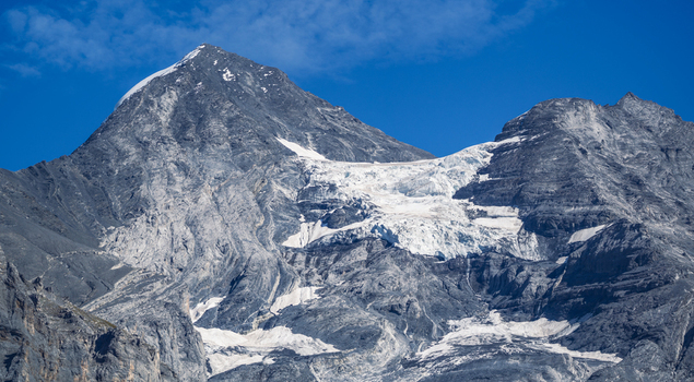 Aerial view of a snow capped mountain peak and glacier with rugged rocky slopes under a clear blue sky in Kandersteg Canton of Bern Switzerland. Aerial view of a snow capped mountain peak and glacier with rugged rocky slopes under a clear blue sky in Kandersteg Canton of Bern Switzerland.