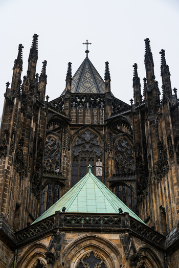 View of the intricate Gothic architecture of St. Vitus Cathedral featuring dark stone spires stained glass windows and a green copper roof in Prague Prague Czechia.