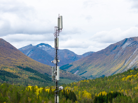 Aerial view of a telecommunications tower standing amidst a vast landscape of dense pine forests and towering mountains under a cloudy sky in Fjord More og Romsdal Norway.
