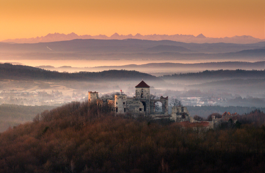 Aerial view of the Krakow Czestochowa Upland featuring historic castle ruins on a forested hill above a misty valley at sunset Krakow County Lesser Poland Voivodeship Poland. Aerial view of the Krakow Czestochowa Upland featuring historic castle ruins on a forested hill above a misty valley at sunset Krakow County Lesser Poland Voivodeship Poland.