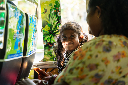 Sri Lanka 31 January 2026 View of a young girl with pigtails smiling while sitting inside a bus with colorful floral seat covers and bright sunlight.