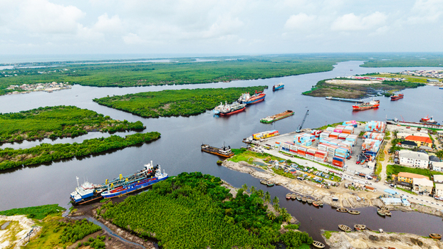 Aerial view of cargo ships shipping containers and lush mangrove vegetation at the port in Satellite Town Lagos Lagos Nigeria.