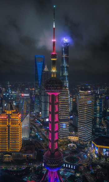 Aerial view of the illuminated Oriental Pearl Tower and Lujiazui financial district skyscrapers under a cloudy night sky in Shanghai Shanghai China.