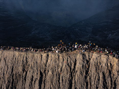 Aerial view of Mount Bromo crater rim with tourists walking along the edge volcanic landscape rugged terrain dramatic shadows in Kecamatan Sukapura Jawa Timur Indonesia.