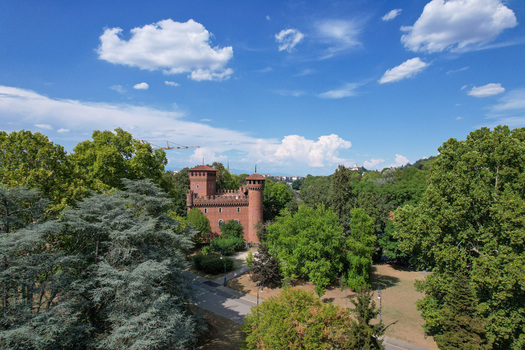 Aerial view of Borgo Medievale castle surrounded by lush green trees and parkland under a blue sky with clouds Torino Piemonte Italy.