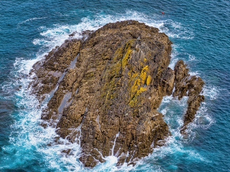 Aerial view of a large rock formation surrounded by crashing waves and turquoise water near Silence Beach Viewpoint in Cudillero Asturias Spain.