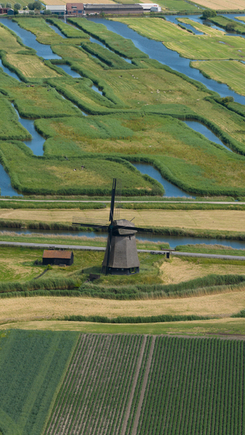 Aerial view of De Museummolen windmill surrounded by lush green polder fields winding canals and agricultural land in Schermerhorn Noord Holland Netherlands. Aerial view of De Museummolen windmill surrounded by lush green polder fields winding canals and agricultural land in Schermerhorn Noord Holland Netherlands.