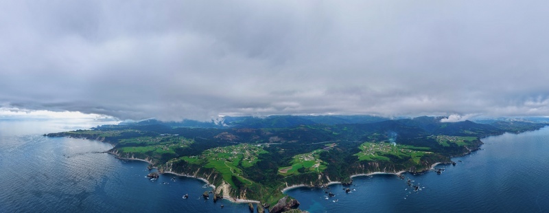 Aerial view of the rugged coastline and lush green hills surrounding the village of Cudillero under a dramatic cloudy sky in Cudillero Asturias Spain. Aerial view of the rugged coastline and lush green hills surrounding the village of Cudillero under a dramatic cloudy sky in Cudillero Asturias Spain.