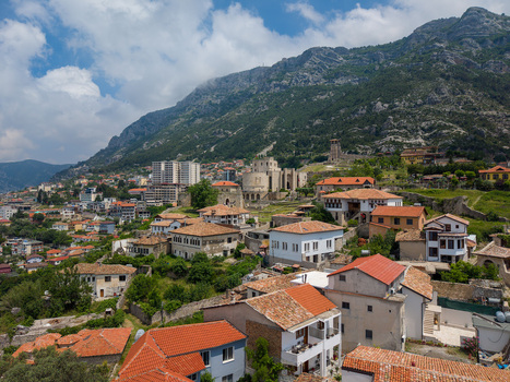 Aerial view of the historic Kruje Castle and traditional red tiled houses nestled at the foot of a rugged mountain under a blue sky in Kruje Durres County Albania.
