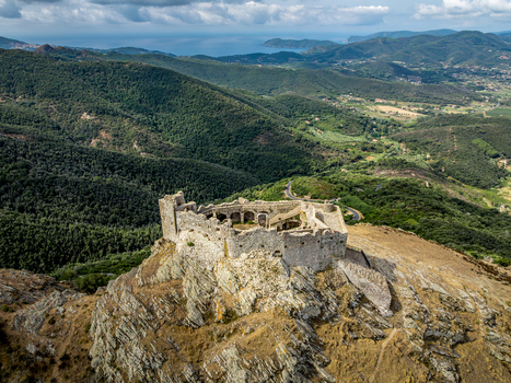 Aerial view of Castello del Volterraio perched on a rocky hilltop surrounded by lush green forests and rolling hills in Portoferraio Toscana Italy.