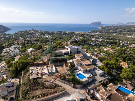 Aerial view of a construction site with a crane next to a modern villa with a swimming pool overlooking the coastal town of Moraira Valencian Community Spain.