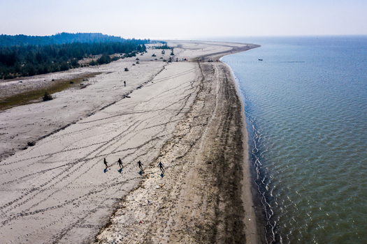 Aerial view of Kuakata beach with people playing soccer on the sand coastline and trees in the background in Kuakata Barisal Division Bangladesh. Aerial view of Kuakata beach with people playing soccer on the sand coastline and trees in the background in Kuakata Barisal Division Bangladesh.