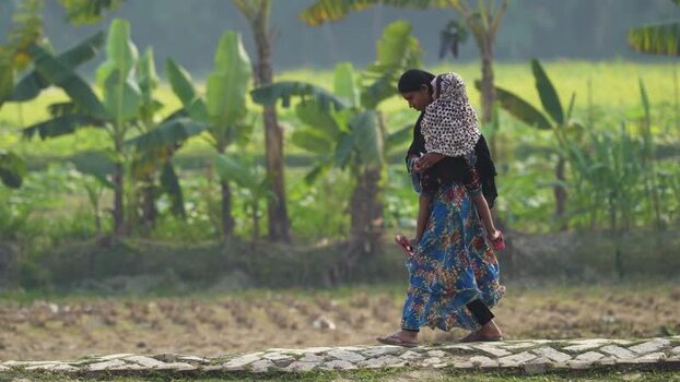View of a woman carrying a child in a rural field Bangladesh.