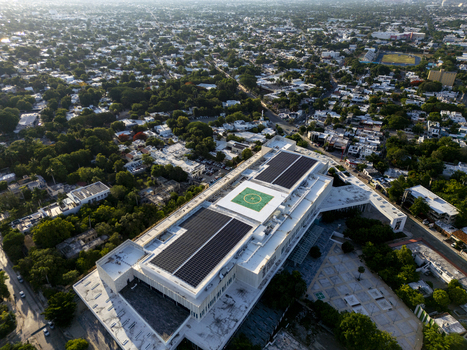Aerial view of Centro Internacional de Congresos de Yucatan featuring solar panels on the roof and a helipad surrounded by urban greenery and city streets in Merida Yucatan Mexico. Aerial view of Centro Internacional de Congresos de Yucatan featuring solar panels on the roof and a helipad surrounded by urban greenery and city streets in Merida Yucatan Mexico.