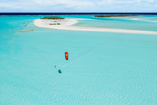 Aerial view of a kitesurfer gliding across the clear turquoise waters of the Aitutaki lagoon surrounded by pristine white sandbars and tropical islands Cook Islands. Aerial view of a kitesurfer gliding across the clear turquoise waters of the Aitutaki lagoon surrounded by pristine white sandbars and tropical islands Cook Islands.