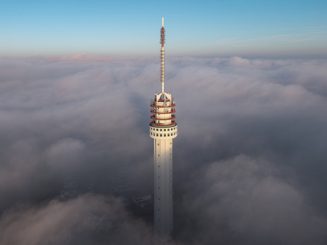 Aerial view of the Zendmast Roermond telecommunications tower rising above a thick layer of low clouds and fog under a clear blue sky in Roermond Limburg Netherlands.