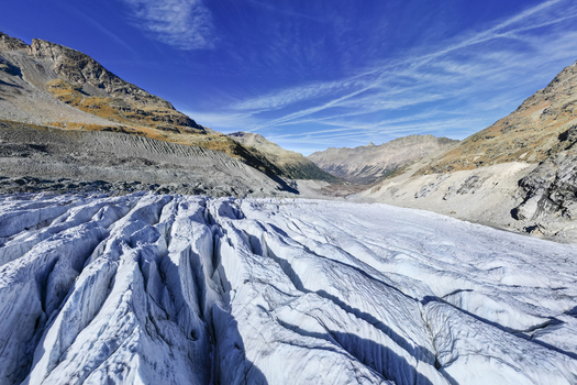 Aerial view of the vast textured Morteratsch Glacier snaking through the rugged rocky valley under a brilliant blue sky Morteratsch Glacier Grisons Switzerland. Aerial view of the vast textured Morteratsch Glacier snaking through the rugged rocky valley under a brilliant blue sky Morteratsch Glacier Grisons Switzerland.