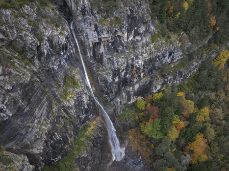 Aerial view of a waterfall cascading down a rocky cliff face in the Pyrenees surrounded by autumn foliage in Spain. Aerial view of a waterfall cascading down a rocky cliff face in the Pyrenees surrounded by autumn foliage in Spain.