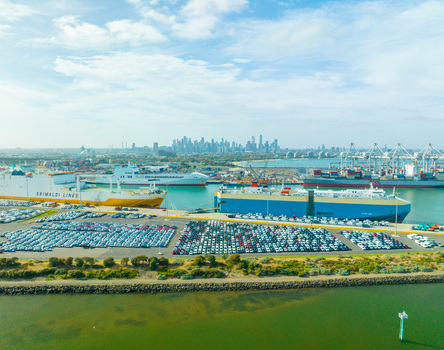 Aerial view of the busy Port of Melbourne with large cargo ships car carriers and vast lots filled with new vehicles with the city skyline in Williamstown Victoria Australia. Aerial view of the busy Port of Melbourne with large cargo ships car carriers and vast lots filled with new vehicles with the city skyline in Williamstown Victoria Australia.