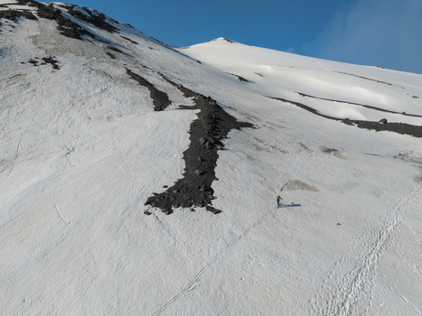 Aerial view of the snow covered south slope of Mount Etna with dark volcanic ash trails and a person walking on the snow Nicolosi Sicilia Italy. Aerial view of the snow covered south slope of Mount Etna with dark volcanic ash trails and a person walking on the snow Nicolosi Sicilia Italy.