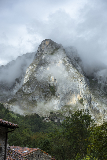 View of a dramatic towering mountain peak shrouded in ethereal clouds juxtaposed against lush verdant foliage Picos de Europa Asturias Spain. View of a dramatic towering mountain peak shrouded in ethereal clouds juxtaposed against lush verdant foliage Picos de Europa Asturias Spain.