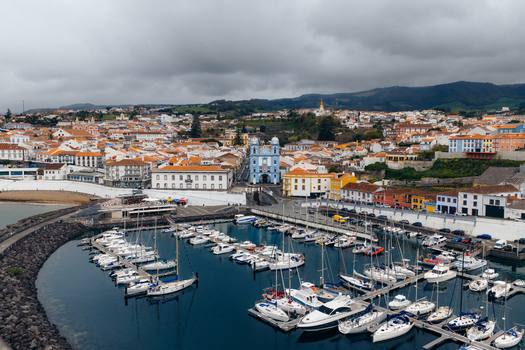 Aerial view of the historic harbor and the blue Igreja da Misericordia church surrounded by traditional orange roofed buildings under a cloudy sky in Angra do Heroismo Azores Portugal.