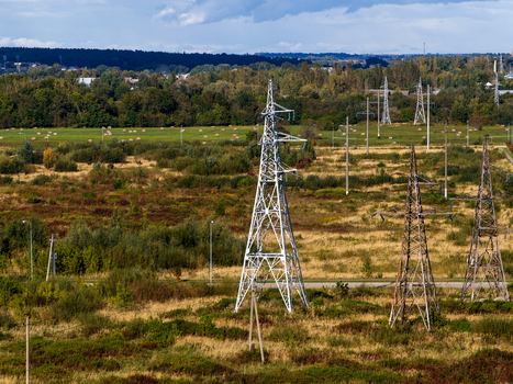 Aerial view of high voltage power lines and electricity pylons crossing a rural landscape with green fields and a dense forest background in Nemencine Vilnius County Lithuania. Aerial view of high voltage power lines and electricity pylons crossing a rural landscape with green fields and a dense forest background in Nemencine Vilnius County Lithuania.
